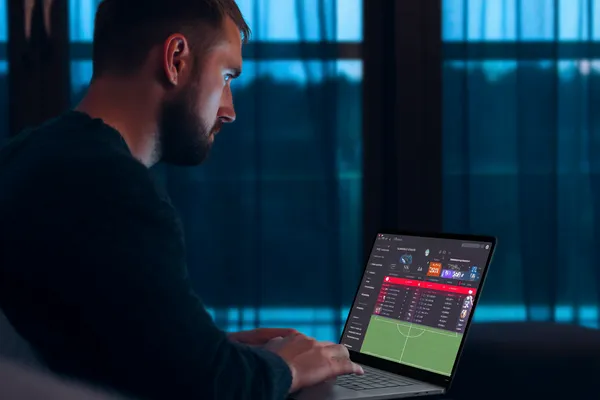 KKDB Mobile App — Your complete hub for casino and sports A man focused on his laptop with live stats in the background, highlighting the dedicated sports and gaming features of the KKDB mobile app.
