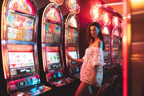 A stylish woman beside vibrant slot machines displaying glowing sevens, showcasing the variety of top slots at KKDB.